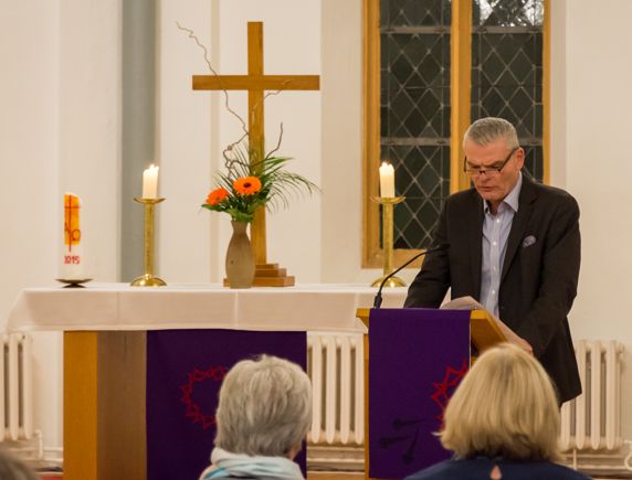 Innenminister Stahlknecht steht vor einem Pult und liest einen Text. Im Hintergrund stehen Kerzen, Blumen und das Kreuz auf dem Altar.